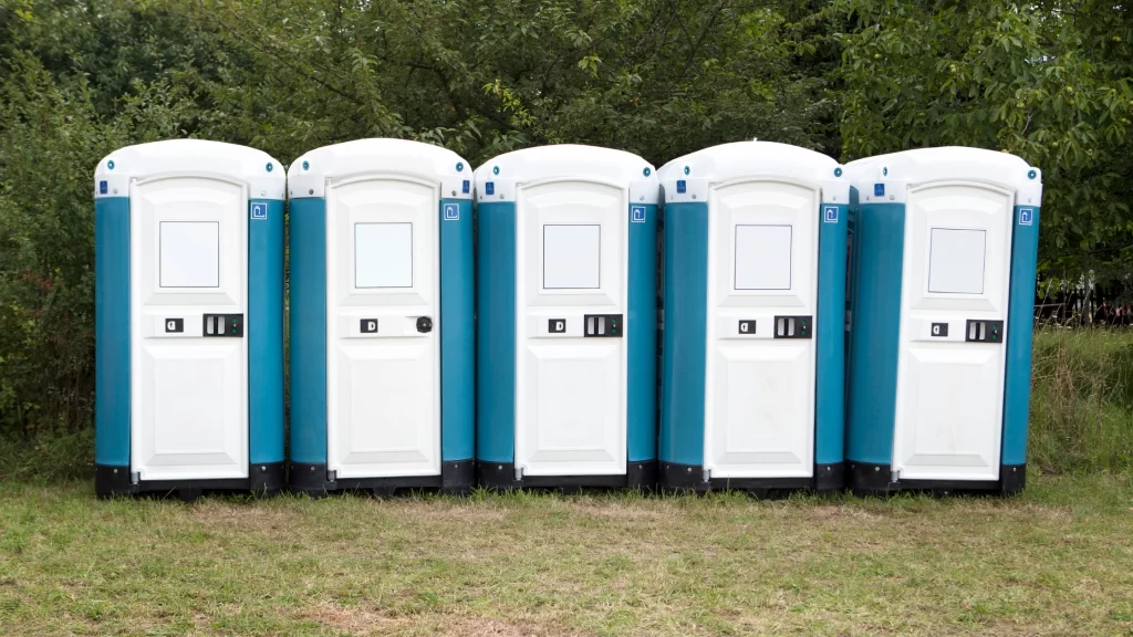 Row of portable toilet rentals lined up outdoors for large events, festivals, and construction site restroom needs.