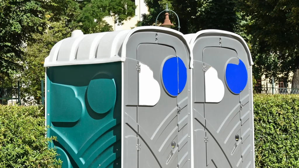 Pair of modern portable restrooms installed in a park setting with trees, ideal for public events and outdoor gatherings.