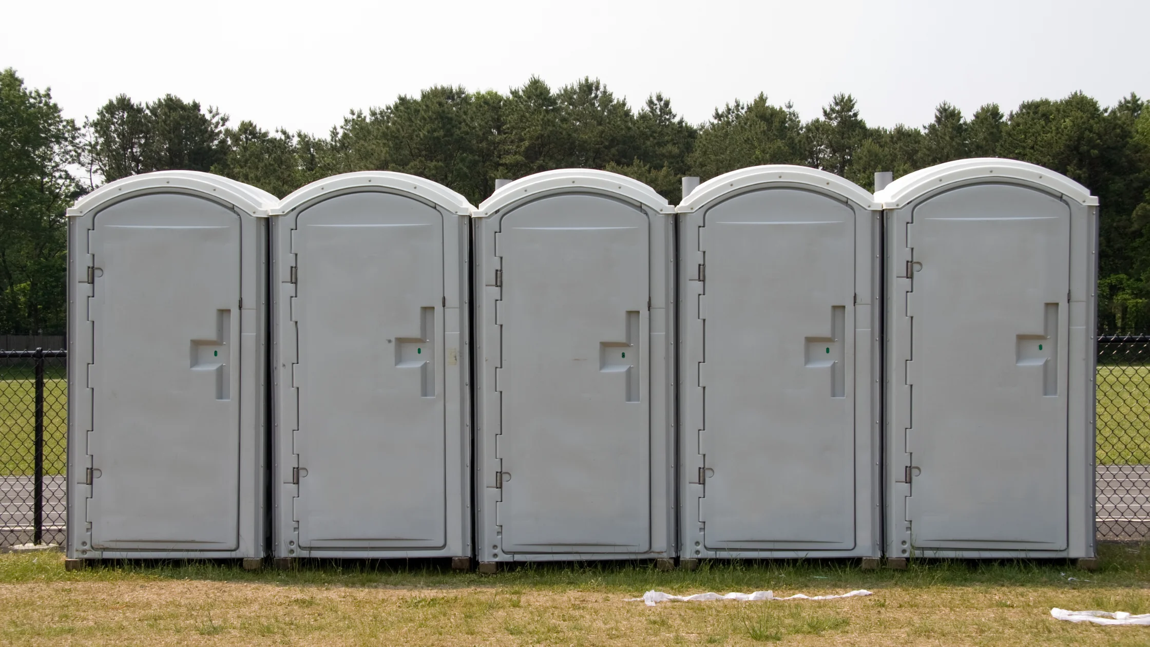 Bathroom rentals near me portable toilet units lined up outdoors for events or construction use.