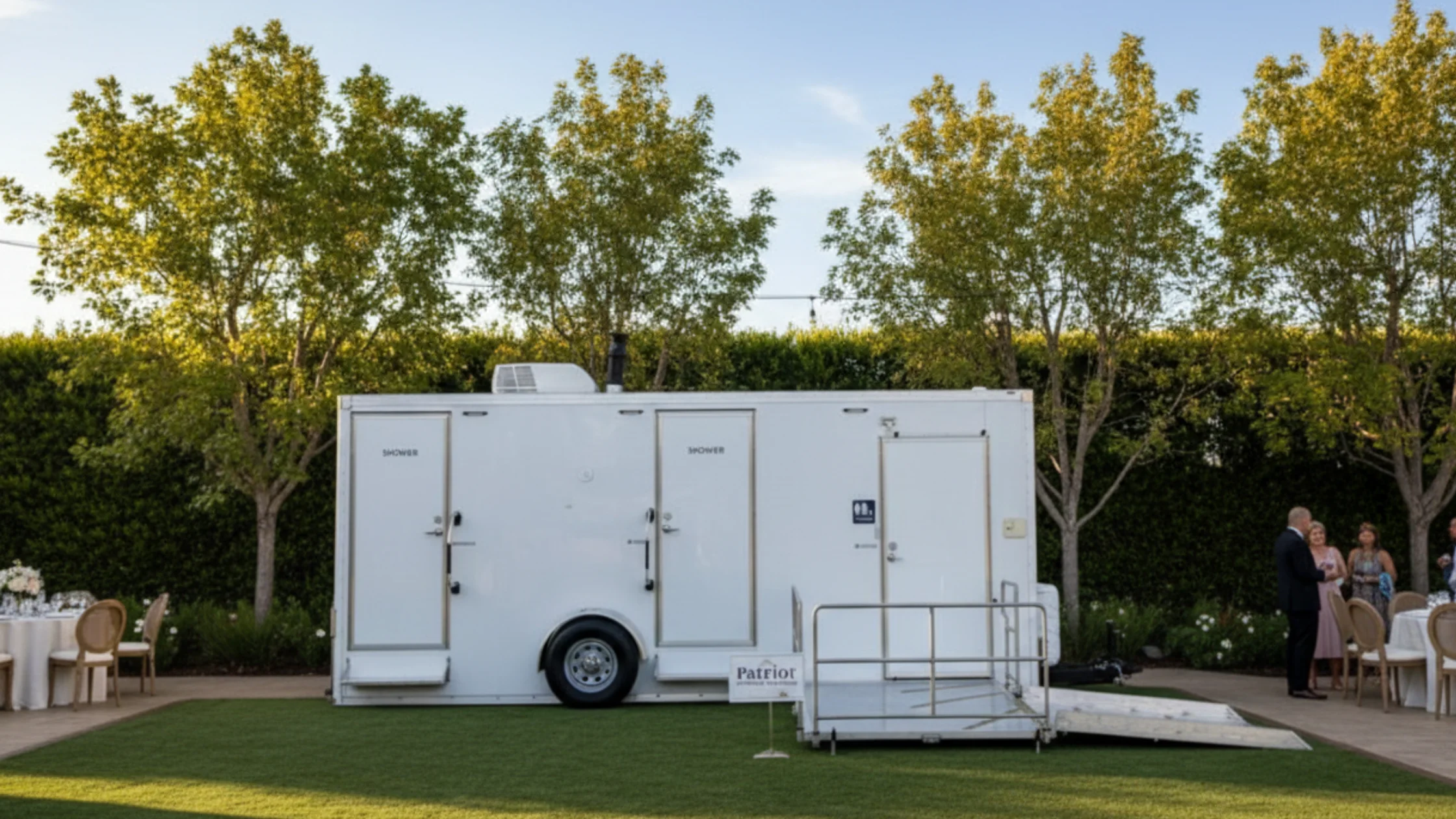 Porta potty rentals mobile restroom trailer set up at outdoor venue with guests nearby.